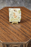Decorative object resembling a miniature book with floral design and 'DIARY' text on a wooden surface.