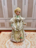 An antique-style 1:12 miniature scale porcelain doll with blonde hair wearing an ornate cream-colored Victorian gown with lace and floral details.