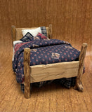 Miniature wooden bed with plaid bedding on a wooden floor.