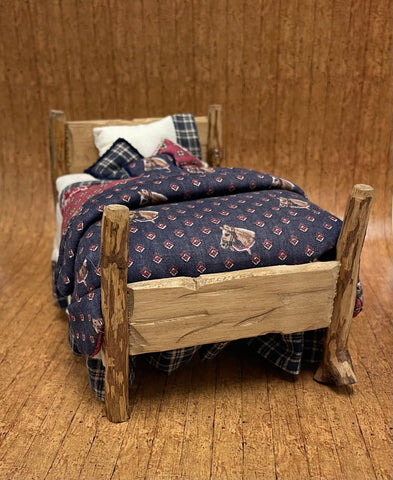 Miniature wooden bed with plaid bedding on a wooden floor.