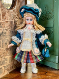 A vintage-style 1:12 miniature scale  porcelain doll with long blonde hair, wearing a blue bonnet, lace-trimmed blue and white jacket, a multicolor plaid skirt, and white shoes. created by artisan Pat Boldt.