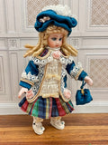 A vintage-style 1:12 miniature scale porcelain doll with blonde hair, wearing a blue hat and coat, lace trim, a multicolor plaid skirt, and holding a small blue bag, created by artisan Pat Boldt.