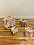 Four 1"12 miniature scale travel cases in a light pink damask pattern with gold-tone hardware