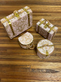 Four miniature vintage-style suitcase and round box containers with a pink damask pattern and gold trim