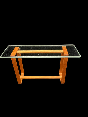 A 1:12 miniature scale modern console table featuring a clear glass rectangular top supported by a warm orange-brown wooden frame with a matching horizontal rail.