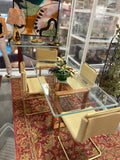 A mid-century modern glass-top dining table with a wooden frame and four matching beige upholstered chairs, set on a red patterned rug inside a showroom.
