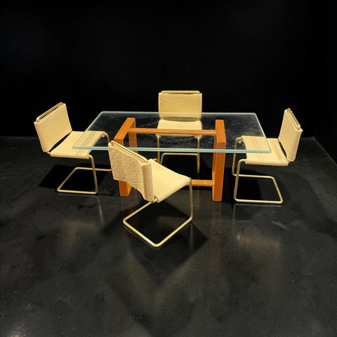 A 1:12 miniature scale modern 5-piece dining set featuring a rectangular glass-top table with a warm orange-brown wooden frame, surrounded by four matching chairs with light tan leather upholstery and gold metal cantilever frames.